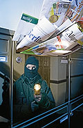 Ein Einbrecher mit Taschenlampe spiegelt sich im Briefkasten, der mit Zeitungen vollgestopft ist